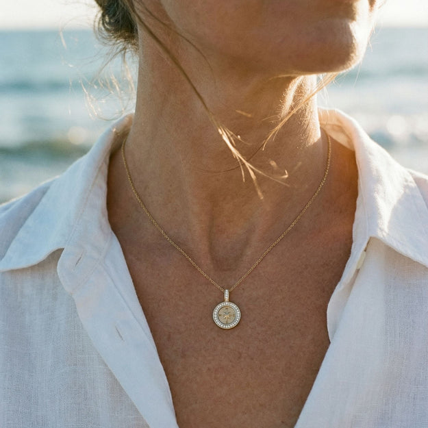 Woman wearing a gold necklace with a pendant by the ocean