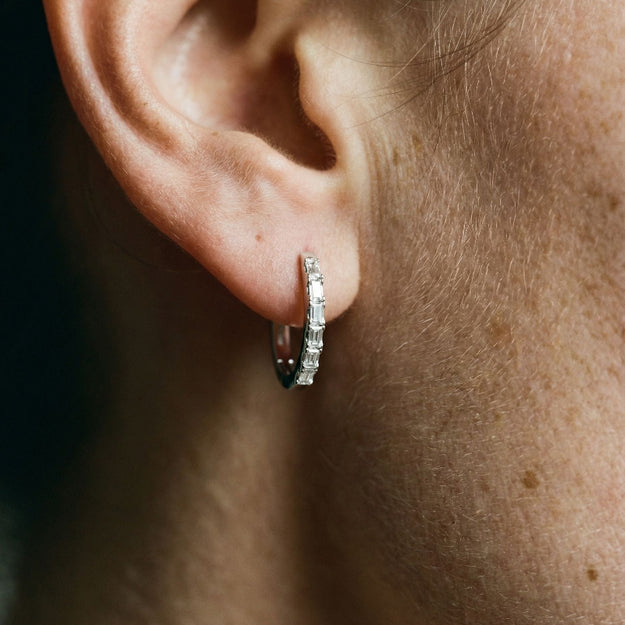 Close-up of an ear wearing a silver hoop earring with clear stones.