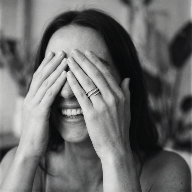 Black and white photo of a woman covering her face with her hands, wearing a ring.