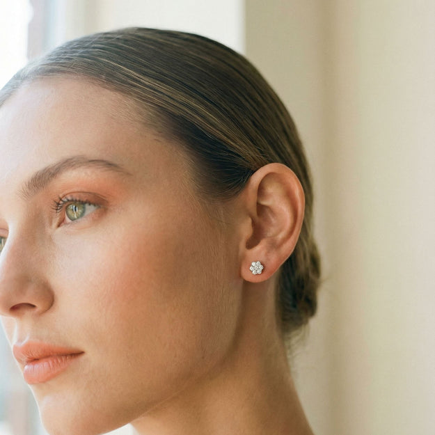 Close-up of a woman wearing diamond stud earrings with a neutral background
