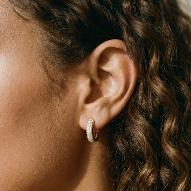 Close-up of an ear wearing a gold hoop earring with soft lighting.