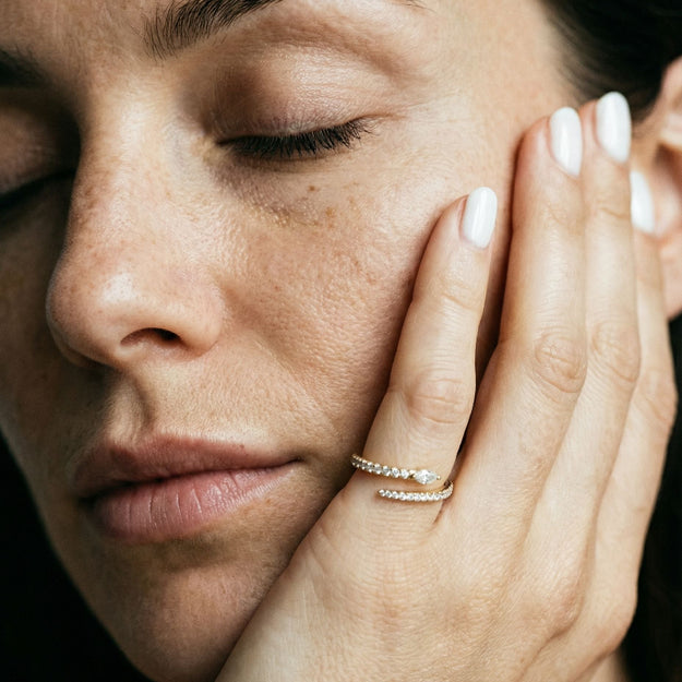 Close-up of a woman's face with her hand near her ear, wearing a ring.