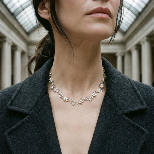 Woman wearing a delicate necklace in an indoor setting with columns.