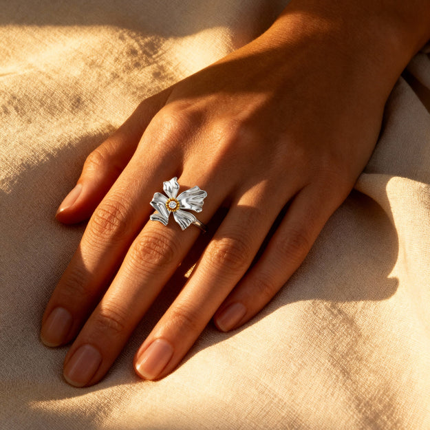 Hand wearing a silver ring with floral design on a beige fabric background