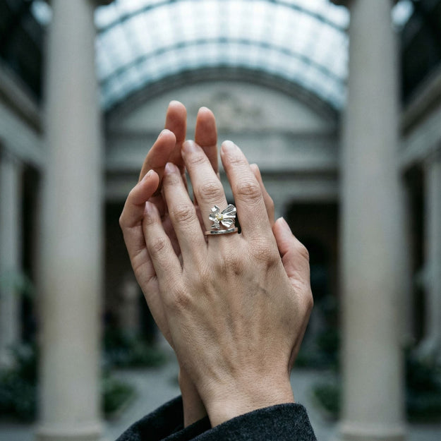 Hand wearing a diamond ring with a blurred architectural background
