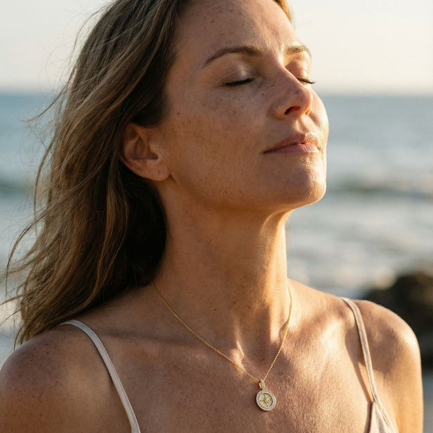 Woman with closed eyes standing on a beach, wearing a necklace.