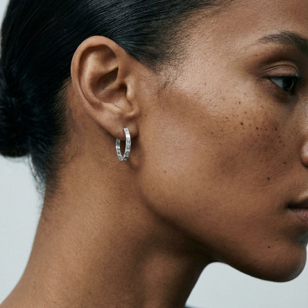Close-up of a person wearing a silver hoop earring against a neutral background