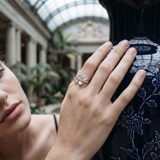 Close-up of a hand wearing a floral ring with an embroidered garment in the background